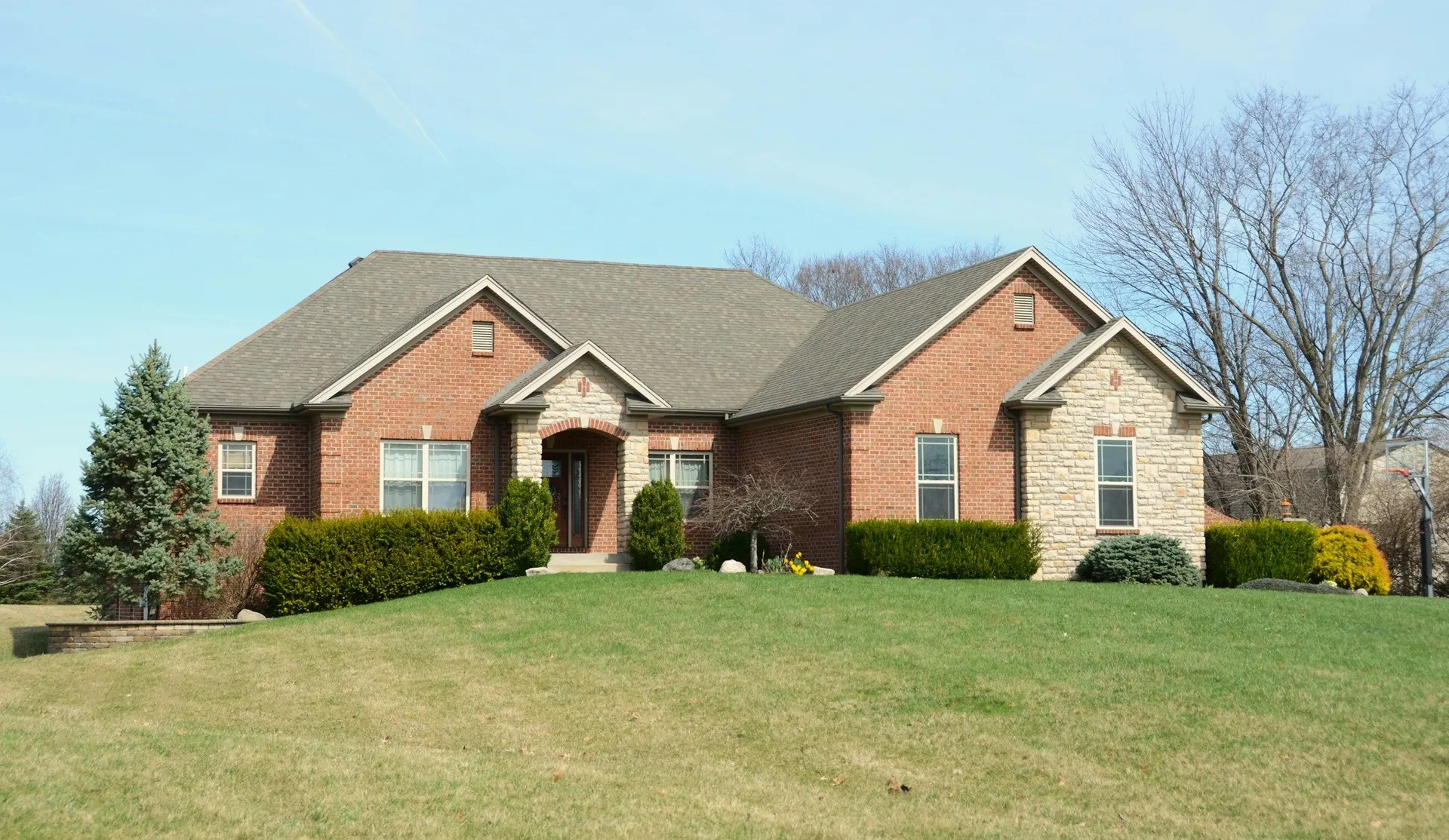 A large brick home on a wide green lawn with trees turning colour behind it