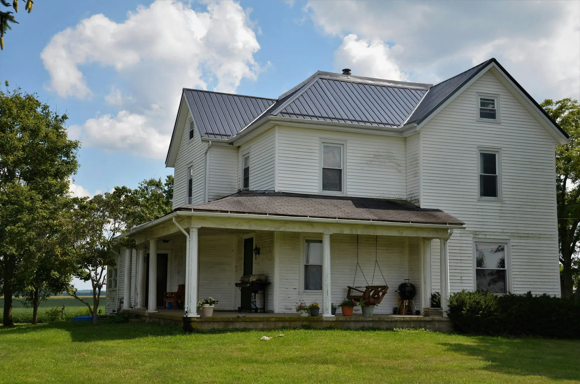 A white two-storey farmhouse with a wraparound porch and a wide lawn