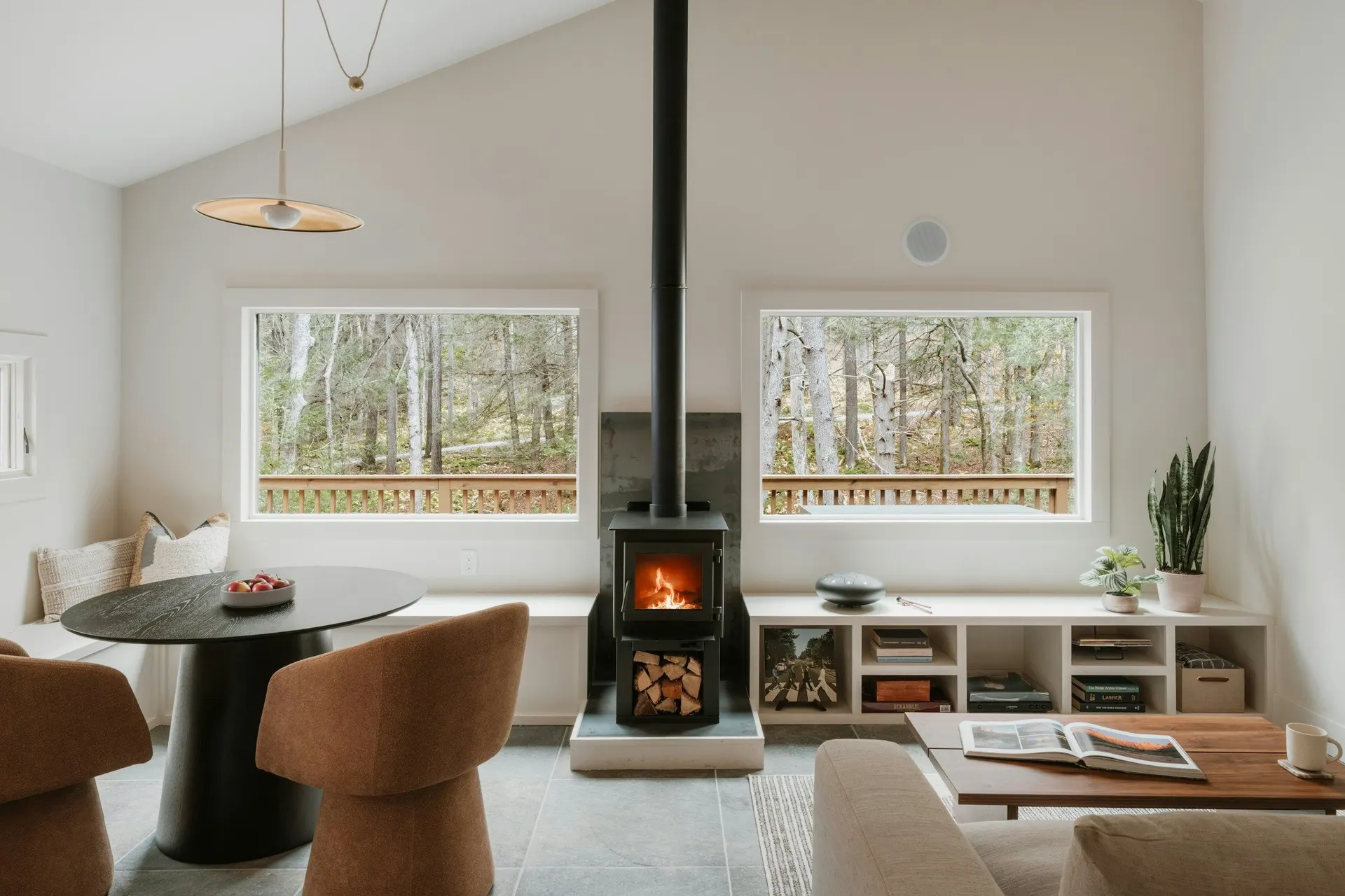 A calm, light-filled living room with a wood stove and two windows onto bare trees