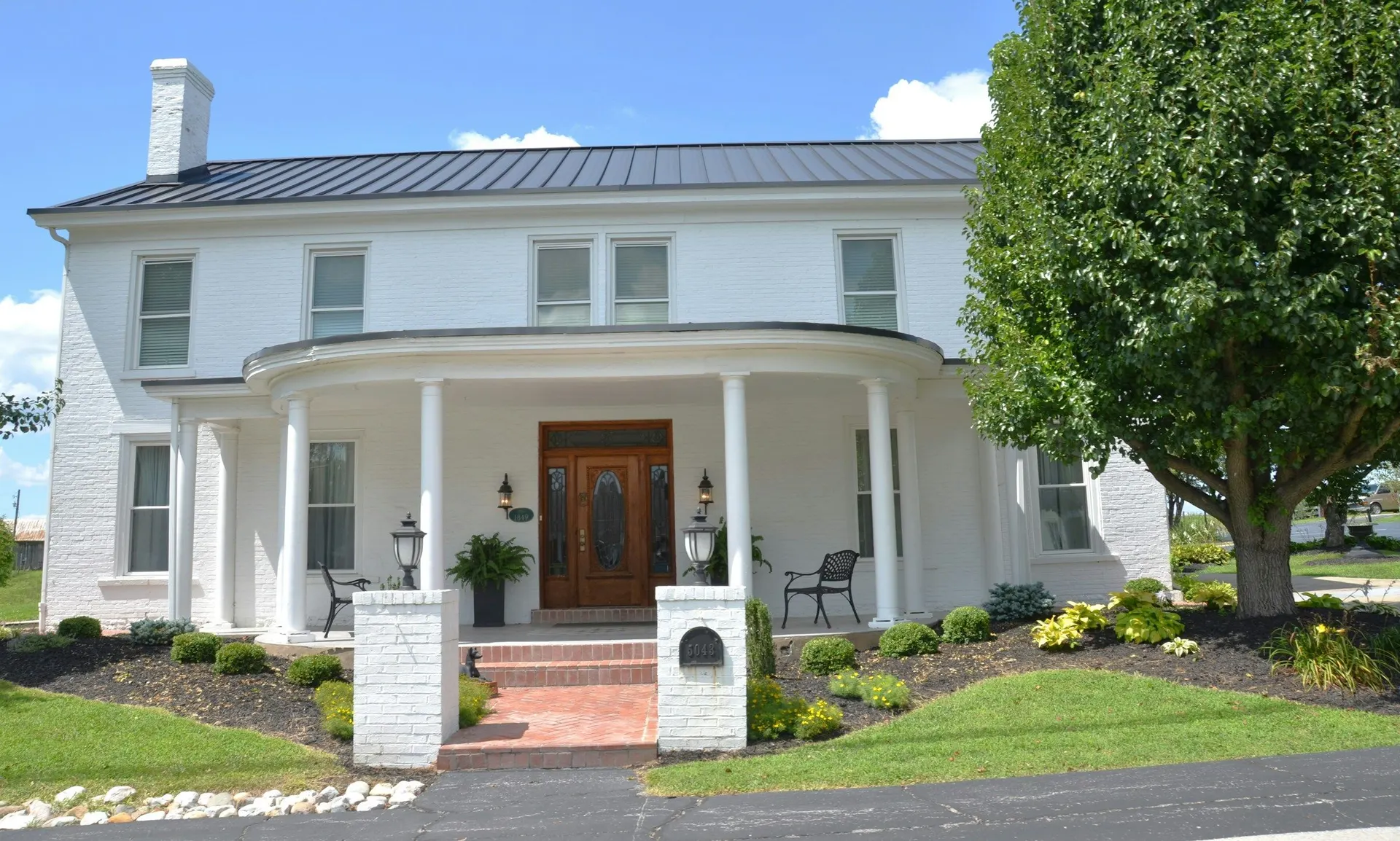 A white painted-brick home with a columned front portico and landscaped beds